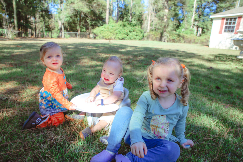 All three Noble children smiling for the camera sitting on lush green grass.